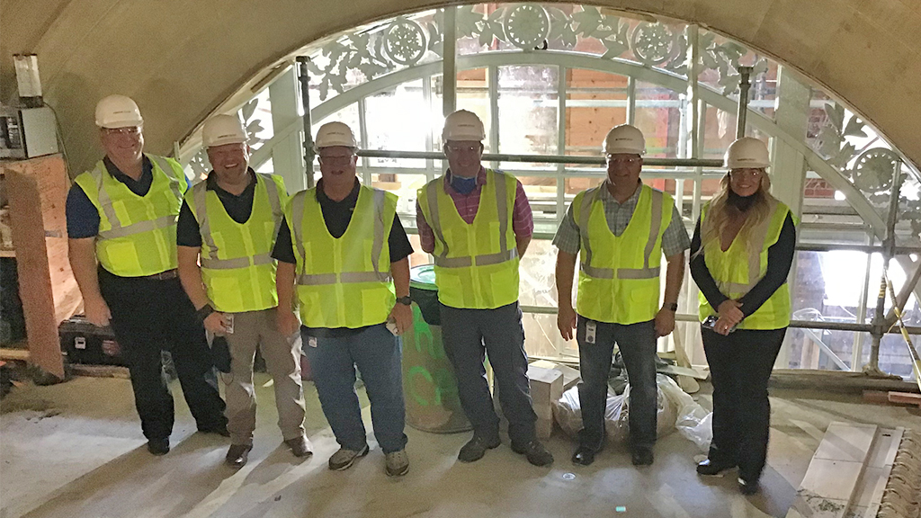 Six construction workers standing by an arch window.